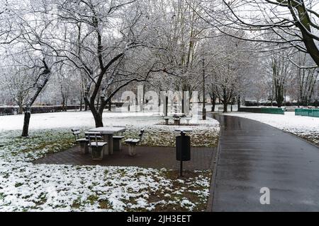 Weitwinkel der Winterszene eines Parks bedeckt mit weißem Schnee mit Bänken vollständig bedeckt während der bewölkten Tageszeit Stockfoto