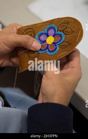 Frau, die in der nördlichen indigenen Gemeinde Deline Blumen auf traditionell gebräuntem Moosleder-Oberleder (für Hausschuhe), einer typischen Dene-Kunstform, reiht Stockfoto