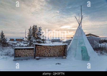 Traditionelles Tipi und Holzstapel im Winter in der nördlichen indigenen Gemeinde Deline, Northwest Territories, Kanada Stockfoto