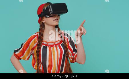 Redhead Mädchen mit Headset Helm App, um Simulation realistisches Spiel zu spielen. Virtual Reality 3D 360-Videofilm ansehen. Junger Teenager Ingwer Kind Kind in VR-Brille isoliert auf blauem Studio-Hintergrund Stockfoto