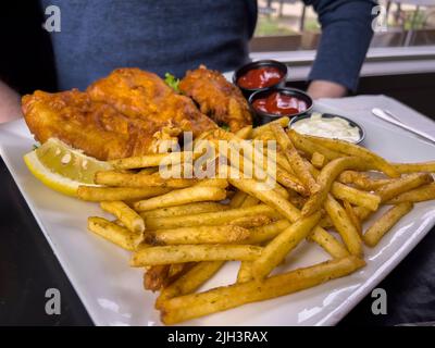 Nahaufnahme von knusprigen Fischen und Chips auf einem Tisch in einem Restaurant vor einem kaukasischen Mann Stockfoto