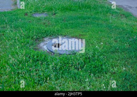 Zerbrochener gusseiserner Schachteleinbruch im Gras im Park. Mannloch mit Loch. Stockfoto