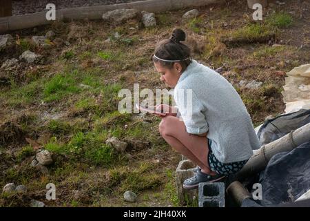 Santa Elena, Antioquia, Kolumbien - Mai 17 2022: Junge Frau in Shorts sitzt in hockender Position und textet auf ihrem Telefon Stockfoto