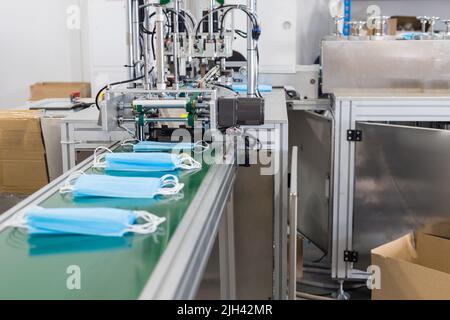 Herstellung von Einweg-medizinischer Kleidung zum Schutz. Medizinische Maske auf dem Förderband in der Fabrik für die Herstellung von medizinischer Kleidung Stockfoto