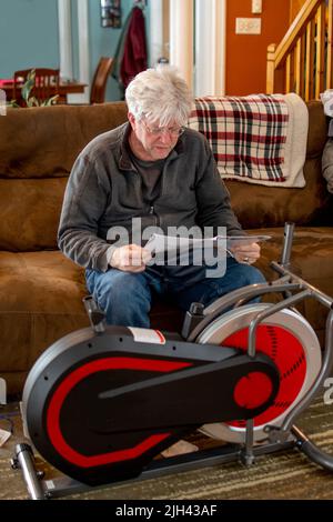 Ein älterer Mann liest Anweisungen, wie man ein neues Heimtrainer zusammenbaut Stockfoto