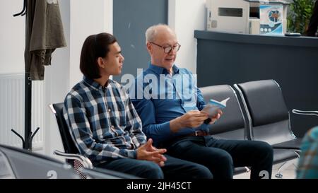 Verschiedene Patientengruppen sitzen auf Stühlen in der Lobby des Warteraum an der Krankenhausrezeption und warten darauf, bei einem medizinischen Termin angerufen zu werden. Menschen mit Krankenversicherung im Wartebereich der Klinik. Stockfoto