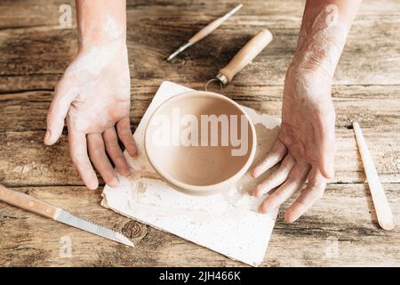 Handwerker Hände mit Töpferwaren und Werkzeugen auf Holz Stockfoto