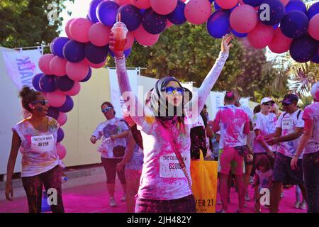 Animierte arabische Frau mit Hijab hebt triumphierend beide Arme nach oben, als sie an einem Ballonbogen-Marker beim Color Walk in Dubai, Vereinigte Arabische Emirate, vorbeikommt. Stockfoto