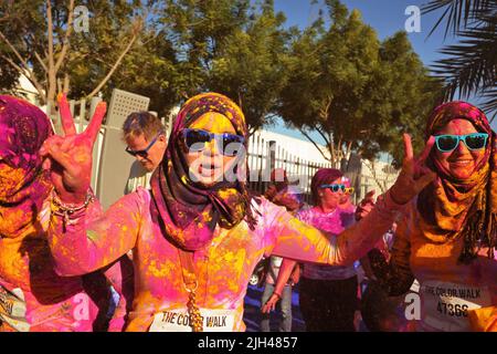 Die mit farbigem Pulver überzogene, animierte arabische Frau mit Hijab- und Blautönen hält beim Color Walk in Dubai, Vereinigte Arabische Emirate, zwei Friedensschilder hoch. Stockfoto