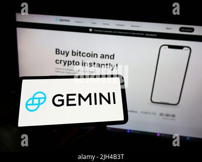 Person, die das Mobiltelefon mit dem Logo des amerikanischen Krypto-Unternehmens Gemini Trust Company LLC auf dem Bildschirm vor der Webseite hält. Konzentrieren Sie sich auf die Telefonanzeige. Stockfoto