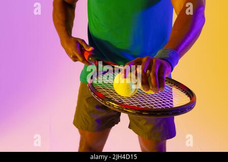 Bild des Mittelteils des afroamerikanischen Tennisspielers in violetter und gelber Neonbeleuchtung Stockfoto