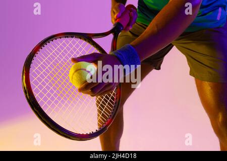 Bild des Mittelteils des afroamerikanischen Tennisspielers in violetter und gelber Neonbeleuchtung Stockfoto