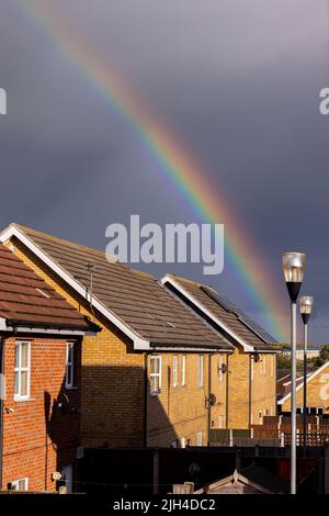 Ein auffälliger Regenbogen sitzt über den Dächern eines Wohnkomplexes, während ein Sturm über den Dächern vorbeizieht. Stockfoto