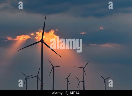 Mallnow, Deutschland. 13.. Juli 2022. Der farbenfrohe Sonnenuntergang scheint durch eine Lücke in den Wolken über den Windenergieanlagen. Quelle: Patrick Pleul/dpa/Alamy Live News Stockfoto