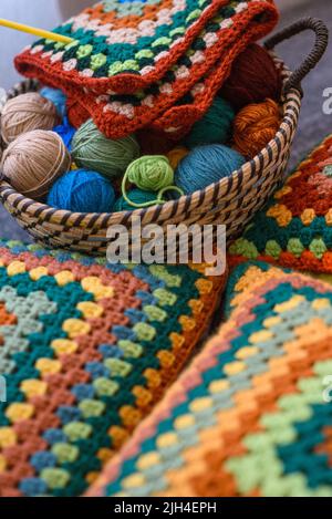 Projekt wird zusammenfügen. Bunte Wollgarne in einem Strohkorb und Strickkissen auf einer Couch. Selektiver Fokus auf Korb. Stockfoto