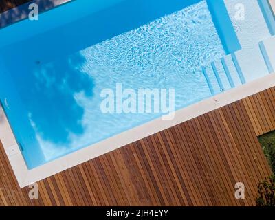 Drohnenflug über den Pool mit schöner Holzterrasse, umgeben von grüner Wiese im schönen Garten Stockfoto