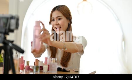 Schöne junge asiatische Make-up-Künstlerin oder Beauty-Bloggerin hält eine kosmetische Serumflasche und nimmt ihr Make-up Tutorial Video auf. Stockfoto