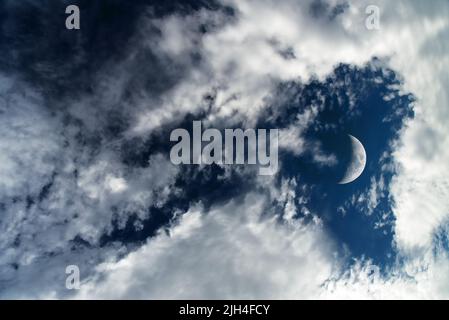 Dunkelblauer dramatischer Himmelshintergrund mit weißen Wolken und Mond. Wunderschöne atmosphärische Wolkenlandschaft. Cumulus Clouds Stockfoto