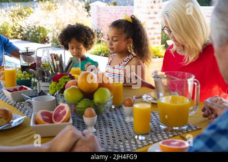 Multirassische Großmutter und Enkelkinder halten sich die Hände und beten vor dem Frühstück am Esstisch Stockfoto