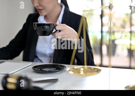 Professionelle asiatische Rechtsanwältin, die in ihrem Büro arbeitet und einen Morgenkaffee schlürft, während sie einen Gesetzesvertrag liest. Zugeschnittenes Bild Stockfoto