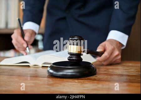 Professioneller und erfolgreicher männlicher Anwalt in formeller Klage, der ein Gesetzbuch liest und an seinem Schreibtisch in seinem Bürozimmer arbeitet. Zugeschnittenes Bild Stockfoto