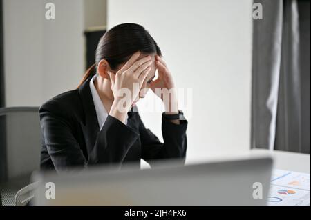 Gestresste junge asiatische Geschäftsfrau oder Finanzarbeiterin, die ein Problem mit ihrer Finanzarbeit hat, Schwierigkeiten bekommt oder sich von ihrem Chef beklagt. Stockfoto