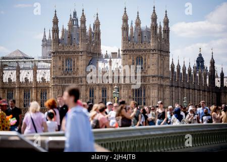 Besucher und Londons überqueren am 14.. Juli 2022 die Westminster Bridge vor der Architektur der britischen Houses of Parliament in London, England. Stockfoto