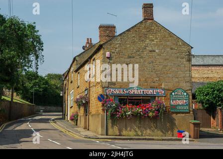 Straßenszene im Sommer im hübschen Dorf Spratton, Northamptonshire, Großbritannien; honigfarbene Steingebäude einschließlich der Metzgerei von Sauls. Stockfoto