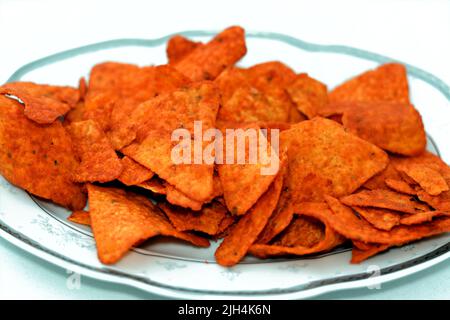 Ein Stapel aromatisierter Tortilla-Chips aus Mais-Tortillas, die in Dreiecke geschnitten und dann gebraten oder gebacken wurden, serviert in einer ovalen Servierplatte, die auf weißem Ba isoliert ist Stockfoto