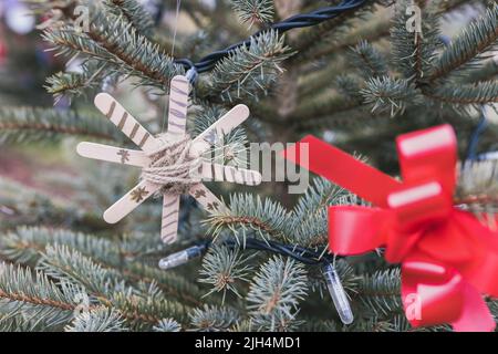 Handgemachte Dekoration auf Weihnachtsbaum im Freien aus Holz Handwerk Eisstäbchen und natürliche Jute Garn. DIY-Ideen für Kinder. Umwelt, Recycling und Zero Waste Konzept. Selektiver Fokus Stockfoto