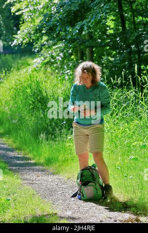 Wandererin, die auf einem Waldweg steht und ihr Mobiltelefon anschaut, Deutschland, Nordrhein-Westfalen, Sauerland Stockfoto