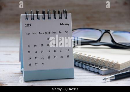 Februar 2023 weißer Tischkalender mit Notizblock und Brillenhintergrund. Konzept und Platz zum Kopieren im neuen Jahr Stockfoto