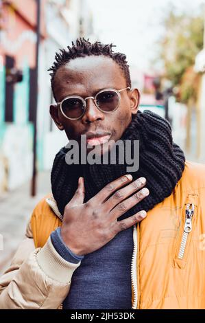 Porträt eines jungen schwarzen afrikanischen Mannes, der Brille und Winterkleidung trägt, auf der städtischen Straße steht, posiert und Kamera anschaut Stockfoto