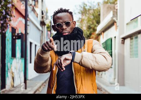 Junger schwarzer afrikanischer Mann, der Winterkleidung trägt, draußen steht, auf die Kamera zeigt und sie anschaut, um zu beginnen. Stockfoto