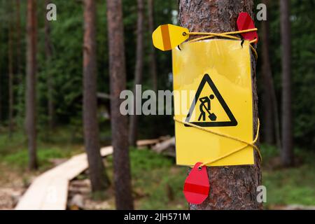 Gelbes Unterbauschild, das an einen Baum mit einer Fahnenlinie in einem finnischen Wald gebunden ist Stockfoto