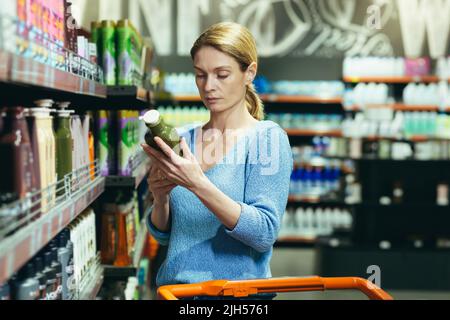Frau wählt und prüft Produkt in den Supermarktregalen. Haushaltschemikalien oder Körperpflegeprodukte Waschmittel im Laden. Frau Kundenhintergrund Stockfoto