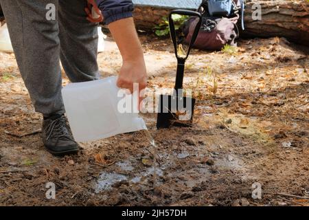 Schwarze Schaufel in menschlichen Händen. Tourist gräbt Erde mit einer Schaufel im Wald. Stockfoto