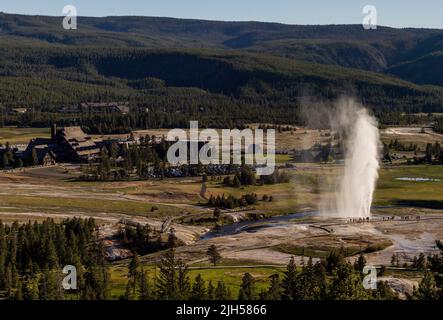 Eine Luftaufnahme des in Aktion explodierenden Bee Hive Geyser vor dem Old Faithful Inn im Yellowstone National Park. Stockfoto