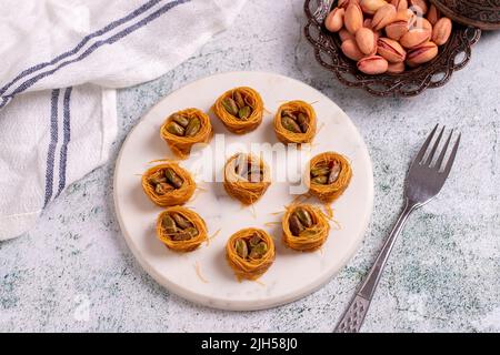 Bulbul Kadayif mit Pistazie. Kadayif Baklava mit Pistazien-Füllung auf einem Steinboden. Türkische Küche, Desserts. Nahaufnahme. Lokaler Name Antep Fıstıklı Stockfoto