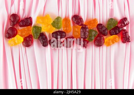 Marmeladentiere verschiedener Farben mit Fruchtsaft liegen auf einem Hintergrund aus zartem rosa Stoff, der mit vielen und dünnen Falten gelegt ist Stockfoto