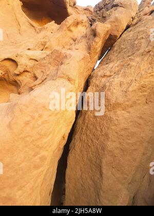 Riesiger Sandsteinfelsen mit einem Riss in der Mitte. Gelbe Kalksteinklippe, die auseinander gerissen hat. Sandsteinwand Hintergrund. Stockfoto