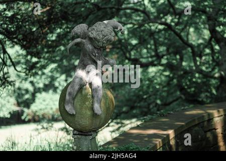 Keramikskulptur eines kleinen sitzenden Engels in einem Botanischen Garten von New Jersey. Stockfoto