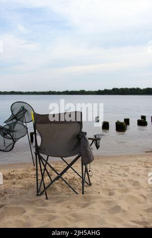 Klappstuhl und Aquarium stehen am Strand. Einzeln angeln. Stockfoto