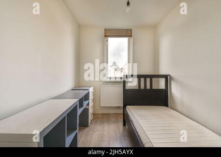 Komfortables Bett in einem kleinen, schmalen, minimalistischen Schlafzimmer mit weißen Wänden und Fenster in einem modernen Apartment Stockfoto