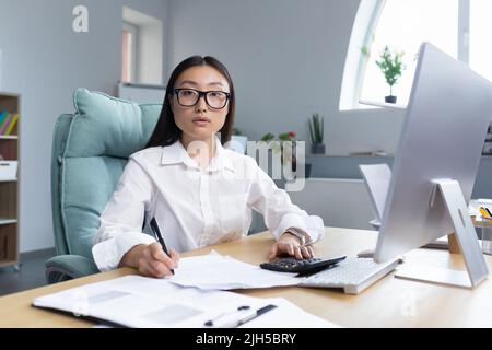 Arbeiten mit Dokumenten. Porträt einer jungen schönen Geschäftsfrau Asiatische Buchhalterin arbeitet mit Dokumenten und Berichten. Am Schreibtisch im Büro sitzend, schreiend, schaut er auf die Kamera. Stockfoto