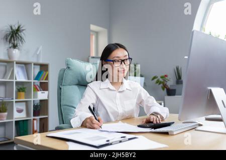 Arbeiten mit Dokumenten. Porträt einer jungen schönen Geschäftsfrau Asiatische Buchhalterin arbeitet mit Dokumenten und Berichten. Am Schreibtisch im Büro sitzen und schreiben. Stockfoto