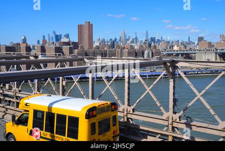 Ein gelber Schulbus, der an einem knackigen Frühlingstag, New York City NY, die ikonische Brooklyn-Brücke überquert Stockfoto