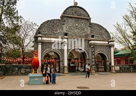 Besuchern stehen neben einer Statue von einem roten Hahn vor dem historischen Eingang in Peking Zoo Stockfoto