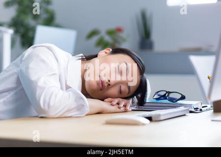 Die junge asiatische Geschäftsfrau schlief am Schreibtisch auf ihren Händen im Büro ein, müde, routinemäßige, langweilige Arbeit, braucht eine Pause. Stockfoto