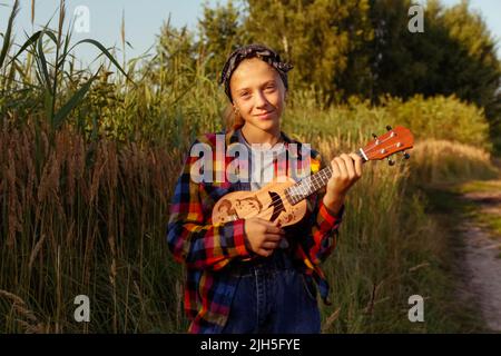 Defokussieren Mädchen mit Gitarre. Teen Mädchen zu Fuß auf Natur Hintergrund. Kleines Mädchen draußen auf grüner Wiese. Generation z. Sommerzeit. Menschen, Musiker. Stockfoto